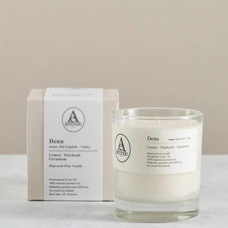 A clear glass jar candle in front of a pale grey candle box