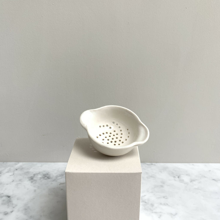 A perforated handmade white tea strainer on a cream box