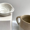 A small white tea strainer next to a mug